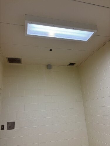 A small sensor mounted high on the wall of a cell beside the ceiling